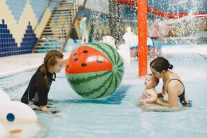 Excursão em parque aquático: tudo o que você precisa saber! | Uma mulher na piscina com uma boia, de frente para outra mulher que segura um bebê | Acquamania